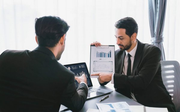 two-men-suits-are-looking-tablet-one-is-holding-chart-that-says-business-plan